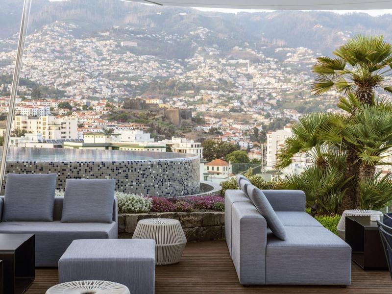 Moderní posezení na terase s výhledem na město a kopce v pozadí.