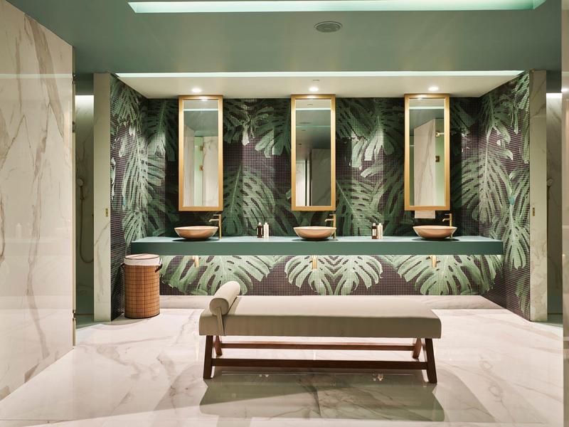Moderní umývárna s tapetou se vzorem listů, třemi zrcadly a dřevěným nábytkem v hotelu.