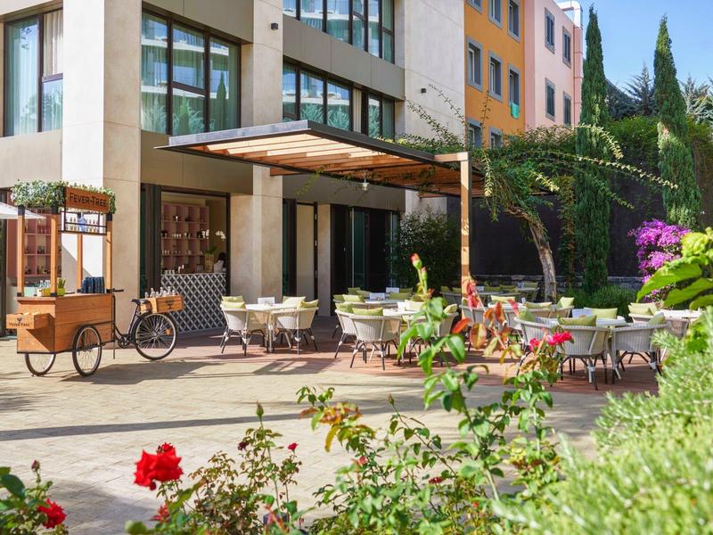 Venkovní prostor hotelu se sezením, rostlinami a dodávkovým vozíkem.