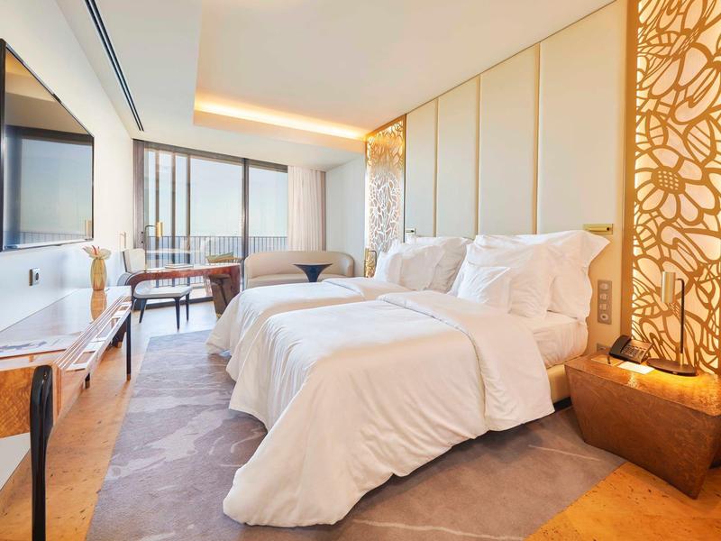 Moderní hotelový pokoj se dvěma jednolůžky, TV, psacím stolem a velkým oknem s výhledem na město.