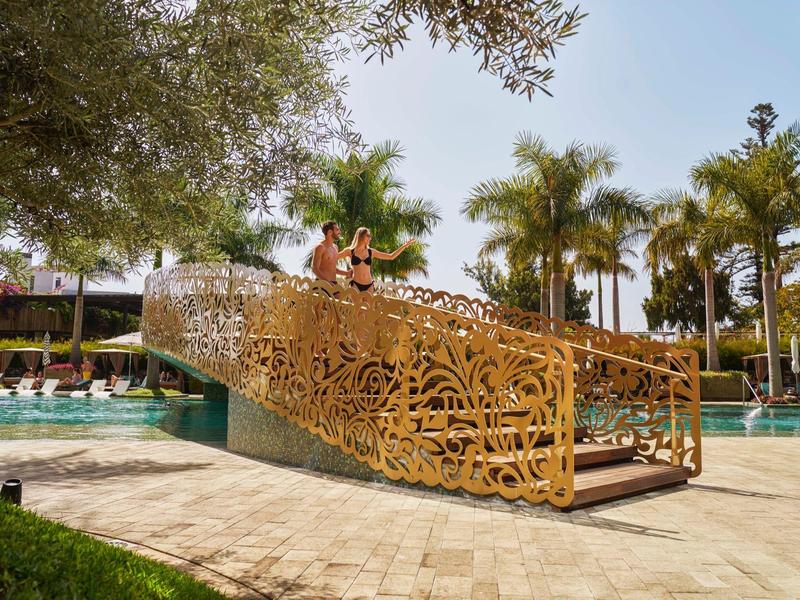 Ozdobený zlatý most přes bazén s palmami v pozadí.