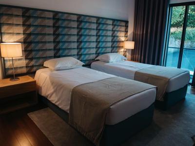 Cozy hotel room with two single beds, bedside tables, lamps, and a balcony door with dark curtains.