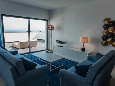 Modern living room with blue sofas, a glass coffee table, ocean view, and sliding glass doors.