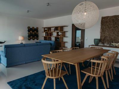 Modern dining and living area with wooden table, chairs, blue sofa, shelves, and large pendant light.