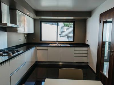 Modern kitchen with white cabinets, black countertops, window with outdoor view, and glass door.