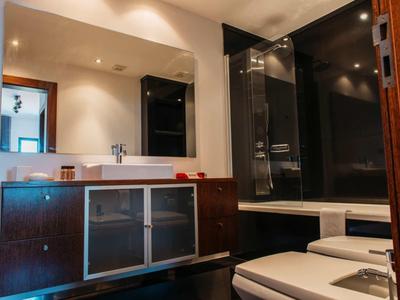 Modern bathroom with dark wood cabinet, white sink, and black-tiled shower area.