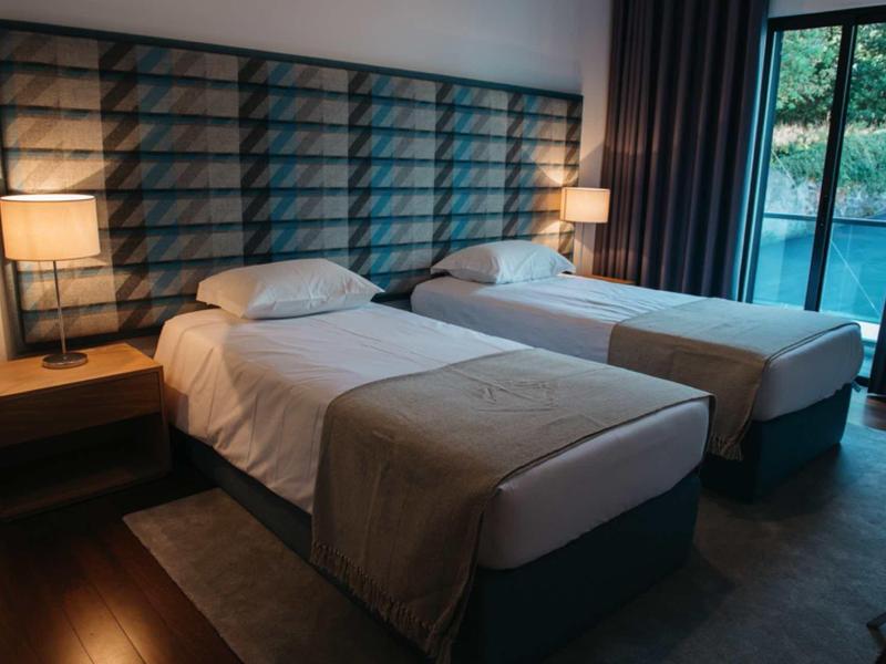 Cozy hotel room with two single beds, bedside tables, lamps, and a balcony door with dark curtains.