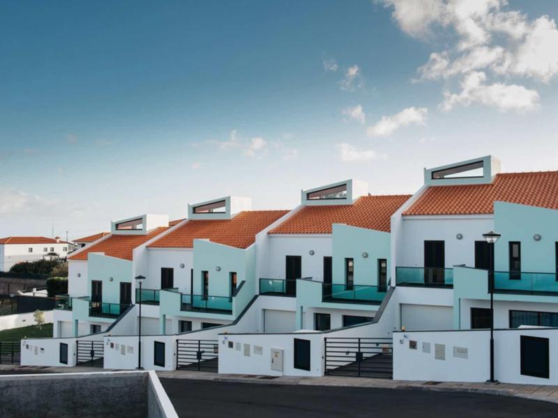 Modern white holiday homes with red roofs and balconies against a partly cloudy sky.