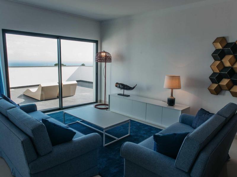 Modern living room with blue sofas, a glass coffee table, ocean view, and sliding glass doors.