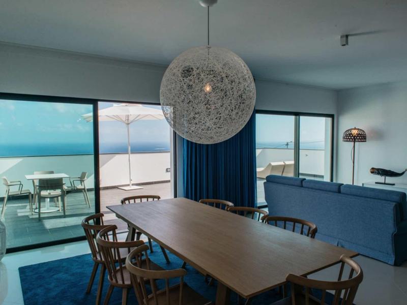 Modern dining room with wooden table, blue chairs, large spherical pendant light, and ocean view patio.