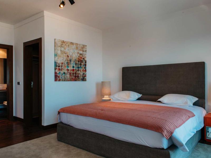Modern hotel room with large bed, coral blanket, bedside lamps, and abstract wall art.