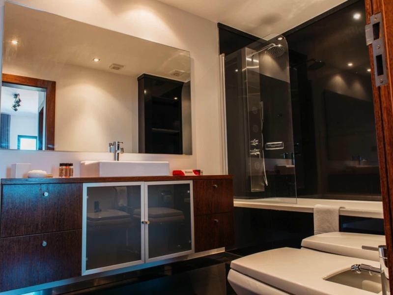 Modern bathroom with dark wood cabinet, white sink, and black-tiled shower area.