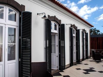 Buitenzijde van een wit gebouw met zwarte luiken en een geplaveide binnenplaats.