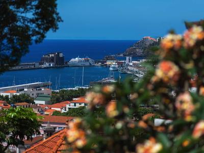 Uitzicht op een haven met schepen, rode daken en blauwe zee bij heldere lucht.