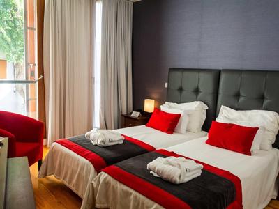 Moderne hotelkamer met twee eenpersoonsbedden, rode kussens en balkonzicht.