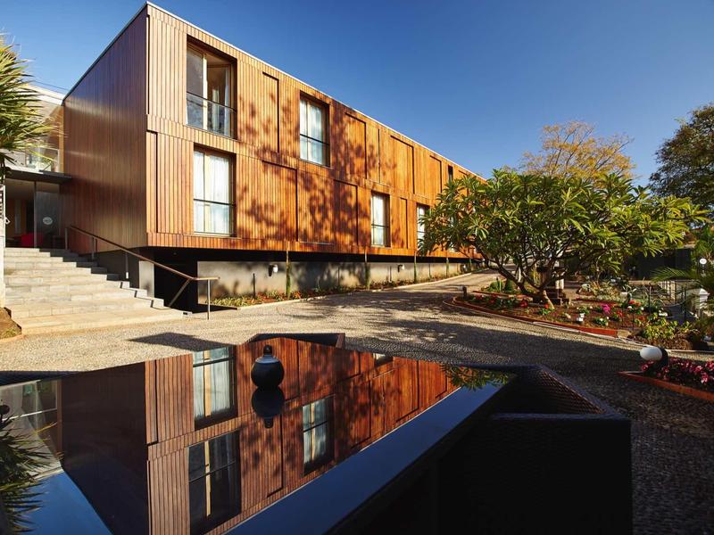 Modern hotelgebouw met houten gevel en reflecterend water op de voorgrond onder een blauwe lucht.
