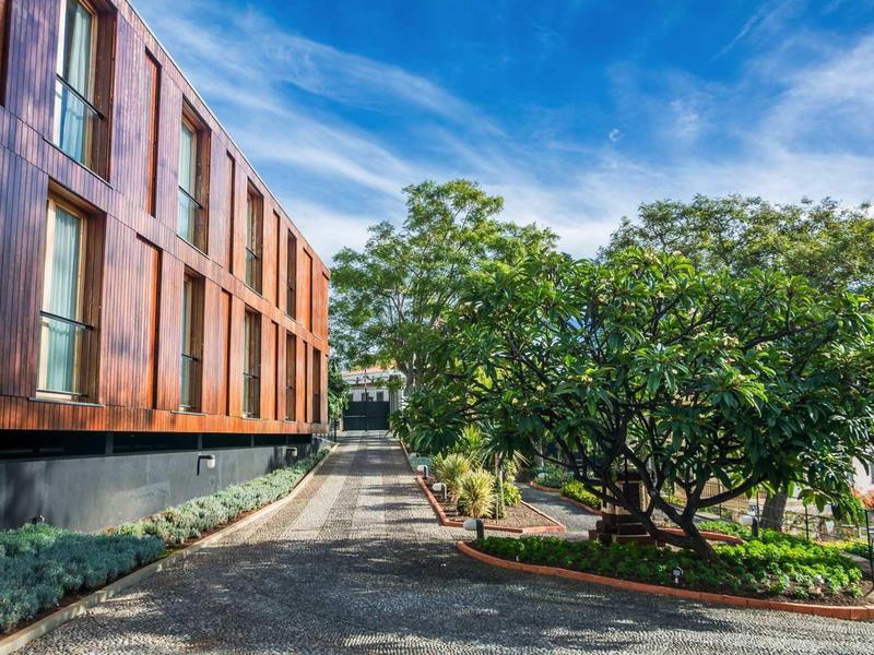Modern hotelgebouw naast een geplaveid pad en grote bomen onder een blauwe lucht.