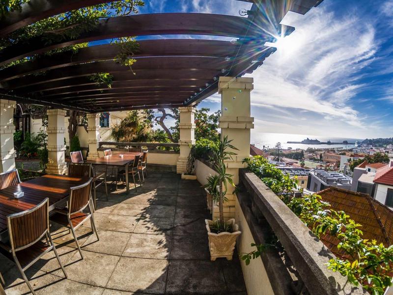 Overdekt terras met tafels en stoelen met uitzicht op de stad en de lucht.