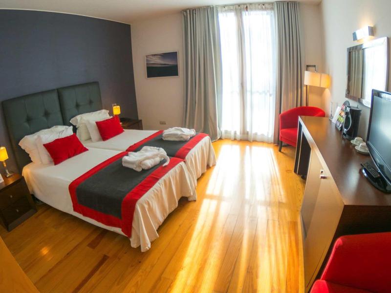 Lichte hotelkamer met twee eenpersoonsbedden, rode accenten en houten vloer.