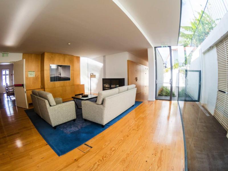 Modern ingerichte woonkamer met houten vloer, blauw vloerkleed en lichte banken bij natuurlijk licht.