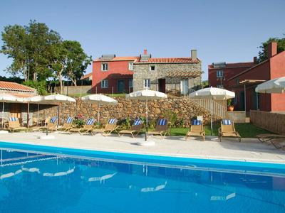 Terrazza dell'hotel con piscina, lettini e ombrelloni davanti a un edificio tradizionale.