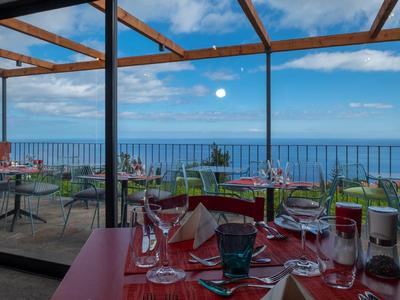 Hotelová terasa s prostřenými stoly a panoramatickým výhledem na moře za jasné oblohy.