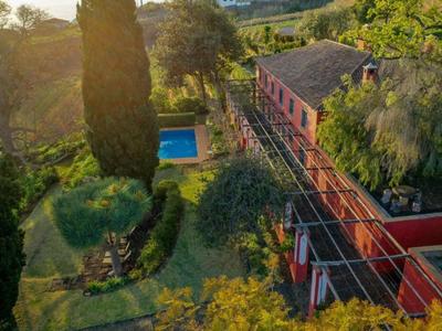 Vista aerea di un edificio rosso con giardino, piscina e alberi al tramonto.