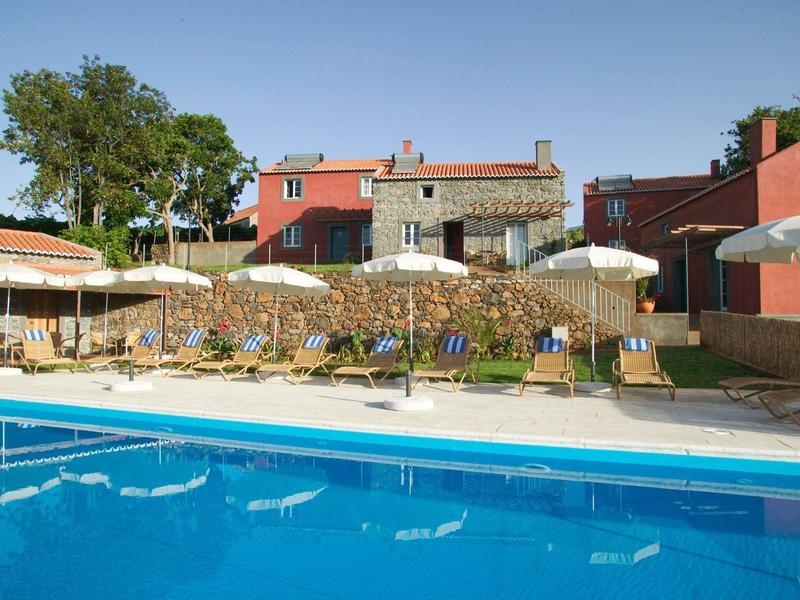 Bazén s lehátky a slunečníky před vícepodlažními domy za slunečného dne.