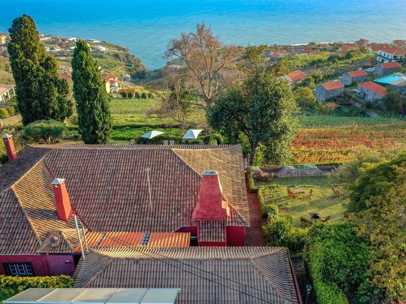 Pohled přes střechy na zelené stromy a pole s modrým mořským horizontem