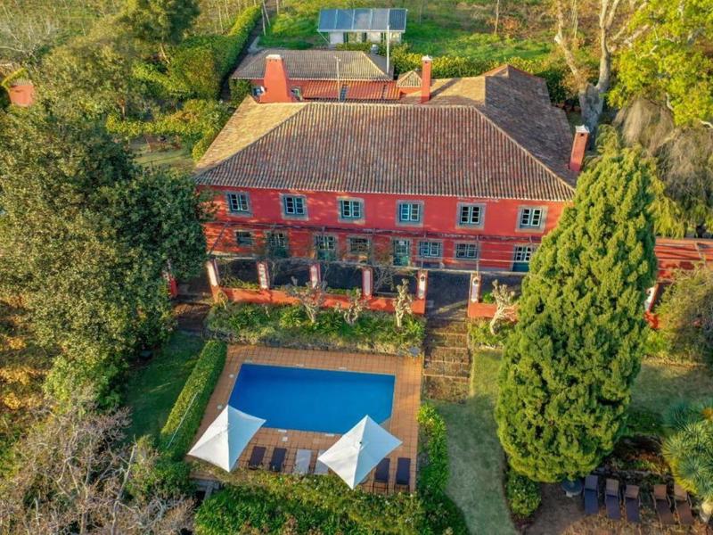 Velký červený venkovský dům s bazénem a okolní zahradou v zelené krajině.