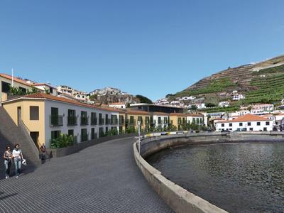 Promenada wzdłuż wybrzeża z domami i wzgórzami w tle pod niebieskim niebem.