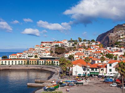 Nadmorskie miasto z czerwonymi dachami i portem pod częściowo pochmurnym niebem.