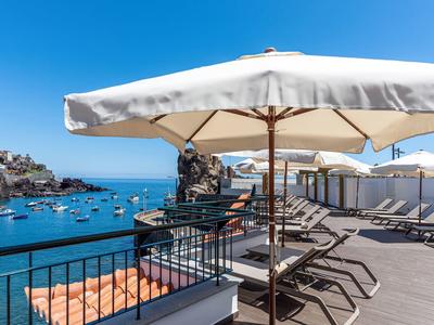Terras met ligstoelen en parasol met uitzicht op haven en boten.