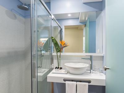 Moderne badkamer met glazen douche, ronde wastafel en verse bloem op het aanrecht.