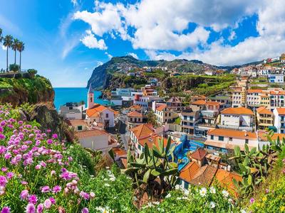 Uitzicht op een kustdorp met kleurrijke huizen, bloeiende bloemen en blauwe lucht.