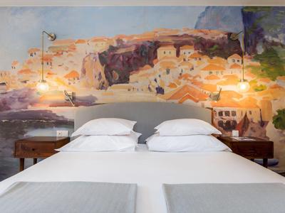 Modern hotelkamer met tweepersoonsbed en muurschildering van een Middellandse Zeestads.