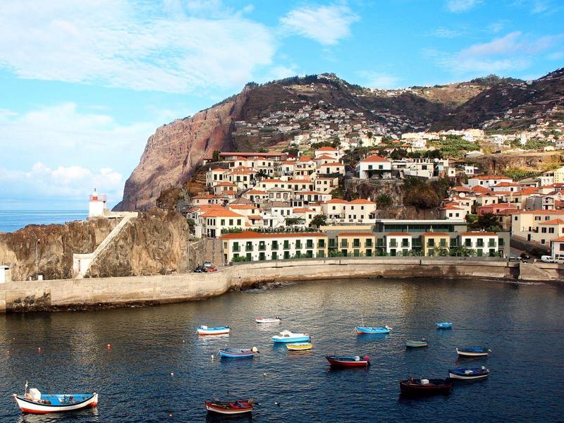 Kuststad met kleurrijke boten in de haven tegen een bergachtige achtergrond en blauwe lucht.
