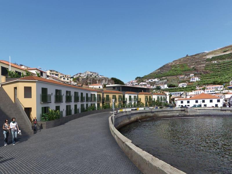Promenade langs een waterkant met gebouwen, heuvels en een heldere lucht op de achtergrond.