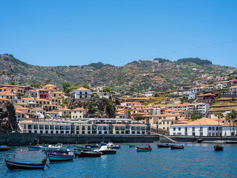 Uitzicht op een kuststad met kleurrijke huizen, boten in het water en heuvels op de achtergrond.