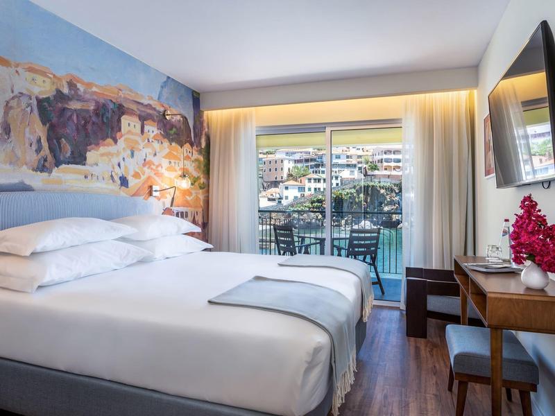 Modern hotelkamer met tweepersoonsbed, grote muurkunst en balkon met uitzicht.