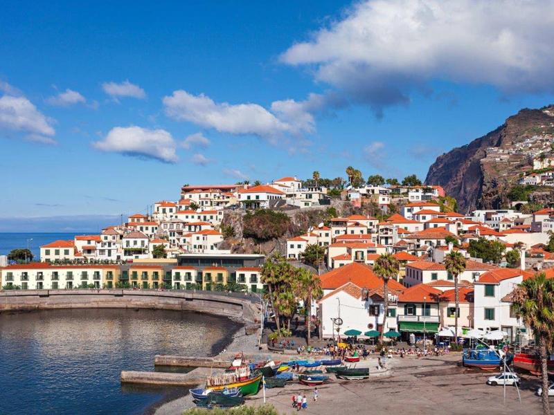 Kuststad met rode daken, blauwe zee en bewolkte lucht op een zonnige dag.