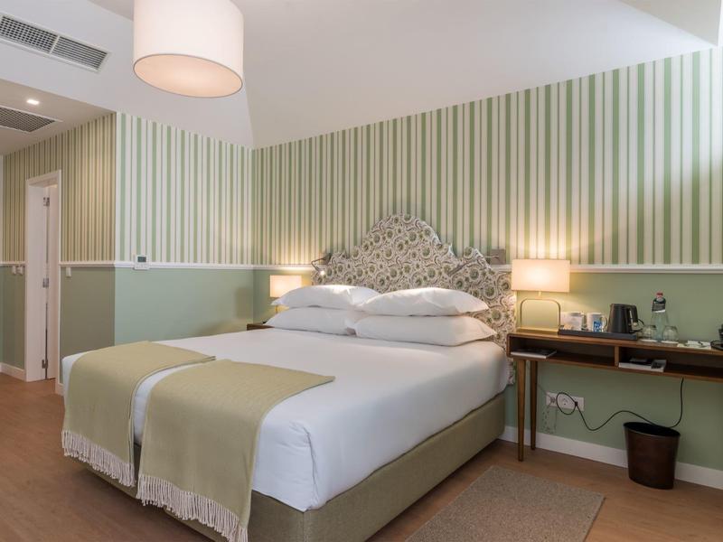 Gezellige hotelkamer met tweepersoonsbed, nachtkastjes en groene muuraccenten.