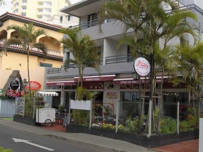 Meerkamerig gebouw met openluchtrestaurant en palmbomen aan een rustige straat.