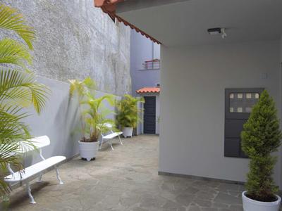 Dvůr s bílými lavičkami, květinami v květináčích a šedými zdmi pod zastřešenou částí.