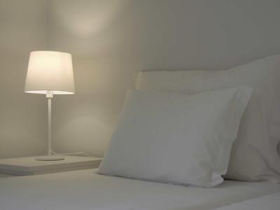 Een eenvoudig wit bed met twee kussens en een stijlvolle lamp op een nachtkastje.