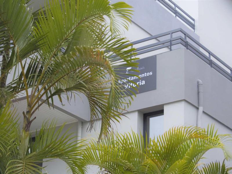 Hoek van een gebouw met grijze muren, hek en groene palmbomen op de voorgrond