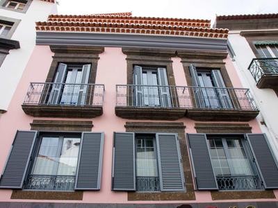 Dettaglio della facciata di un hotel rosa con balconi e persiane in città.