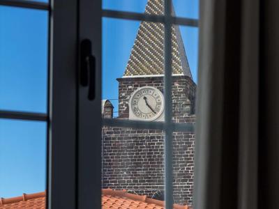 Vista attraverso una finestra su una torre della chiesa con orologio sotto un cielo limpido.