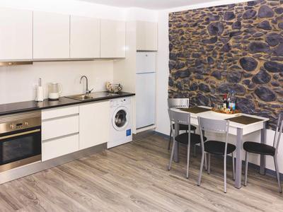 Cucina moderna con armadietti bianchi, lavatrice e tavolo da pranzo davanti a una parete di pietra.