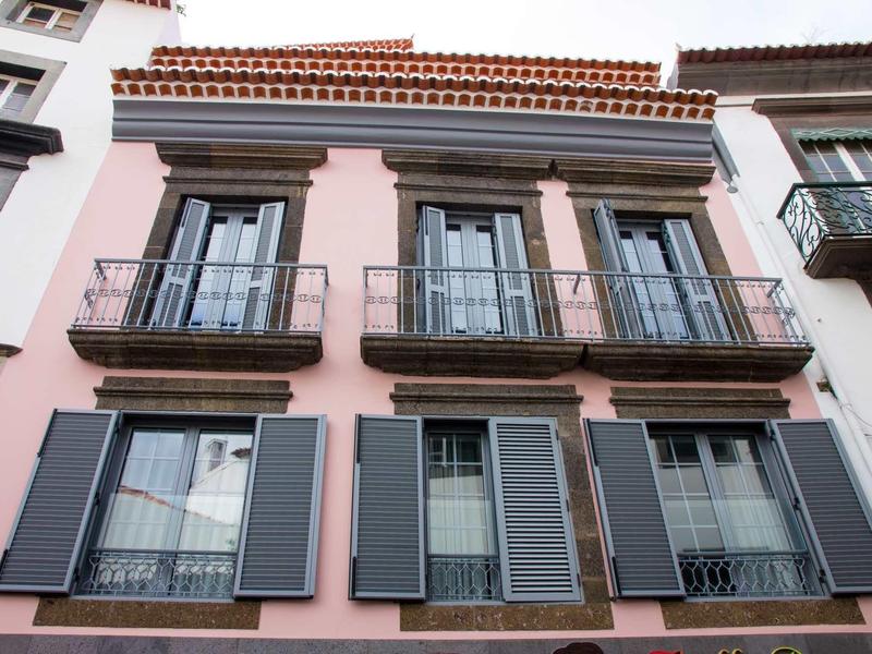 Gevel van een roze hotel met balkons en ramen met grijze luiken